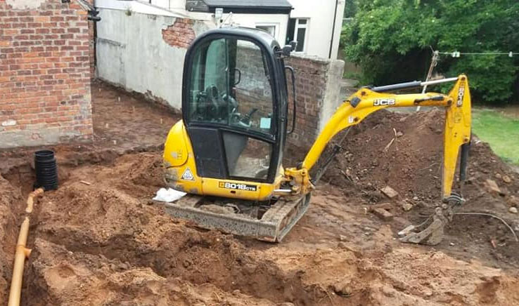 Mini digger digging trench for drainage pipes.